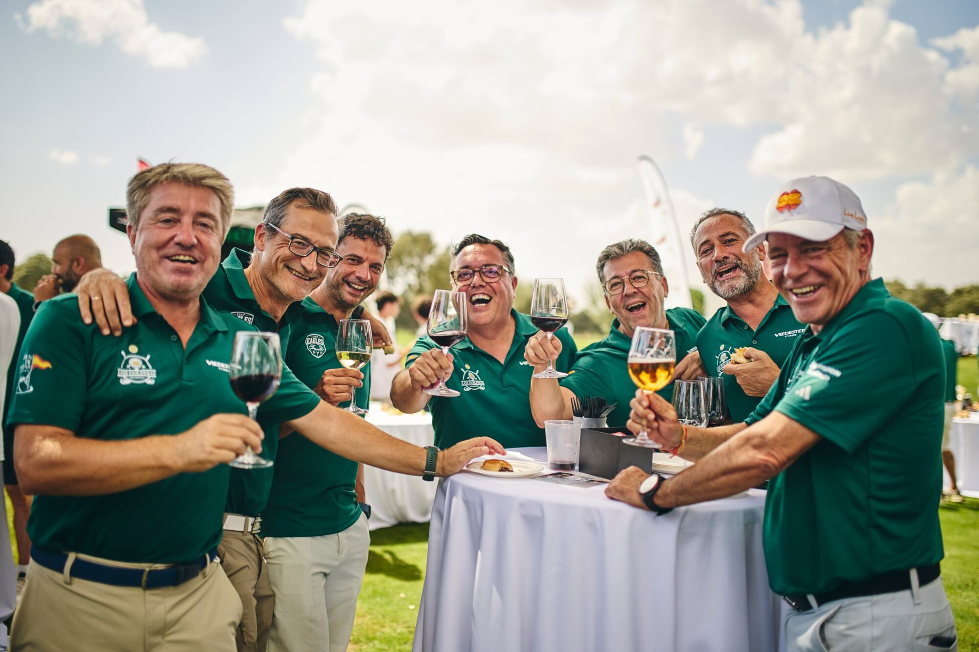 Siete jugadores con el polo verde del torneo brindando alrededor de una mesa alta